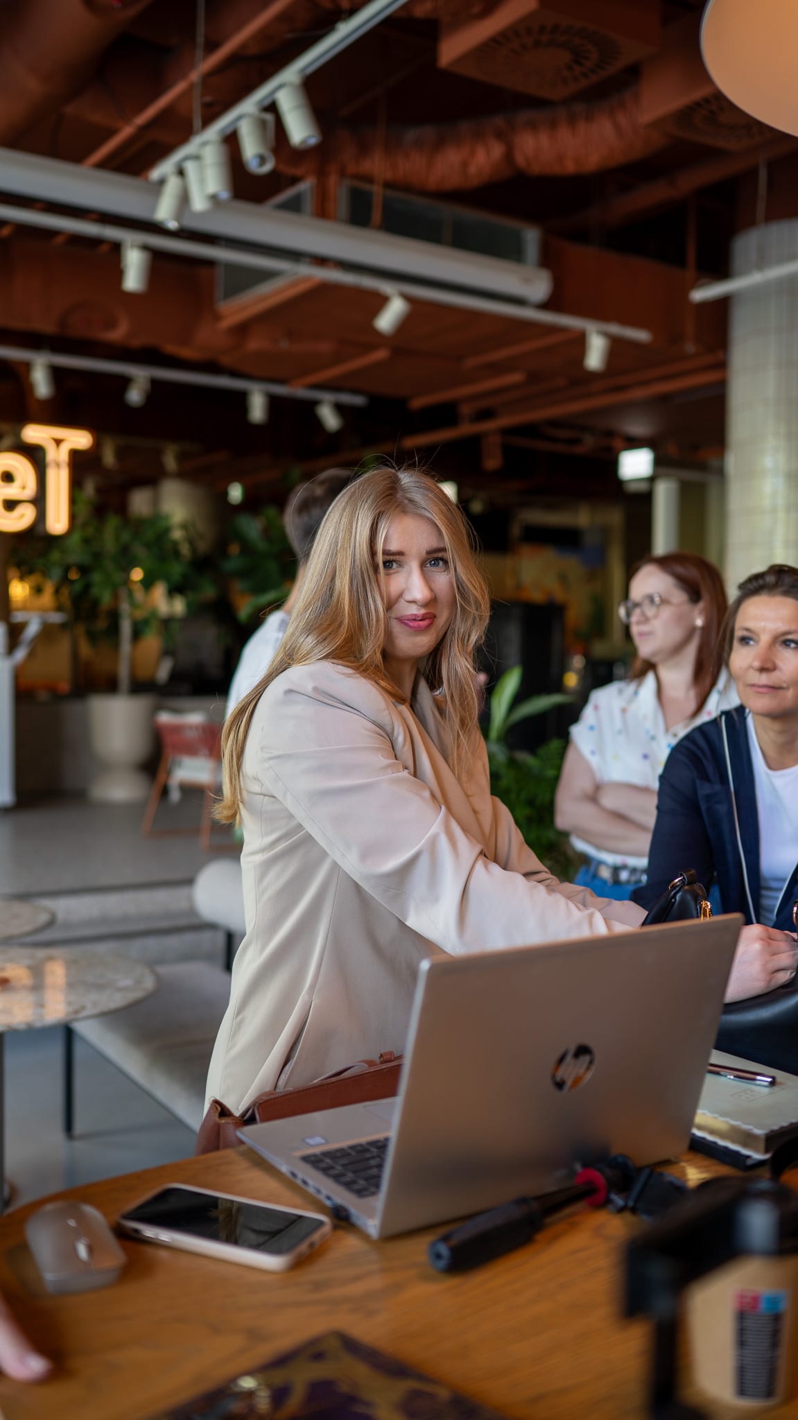Sesja biznesowa — uśmiechnięta kobieta przy laptopie w przestrzeni coworkingowej