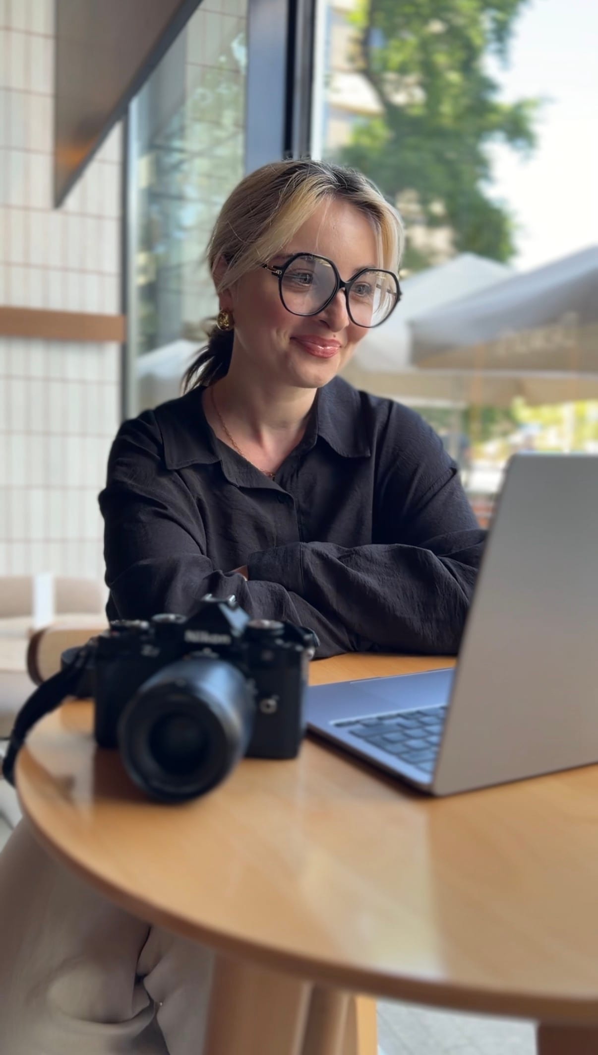 Karolina przy kawiarnianym stoliku z laptopem i aparatem podczas rozmowy przed sesją